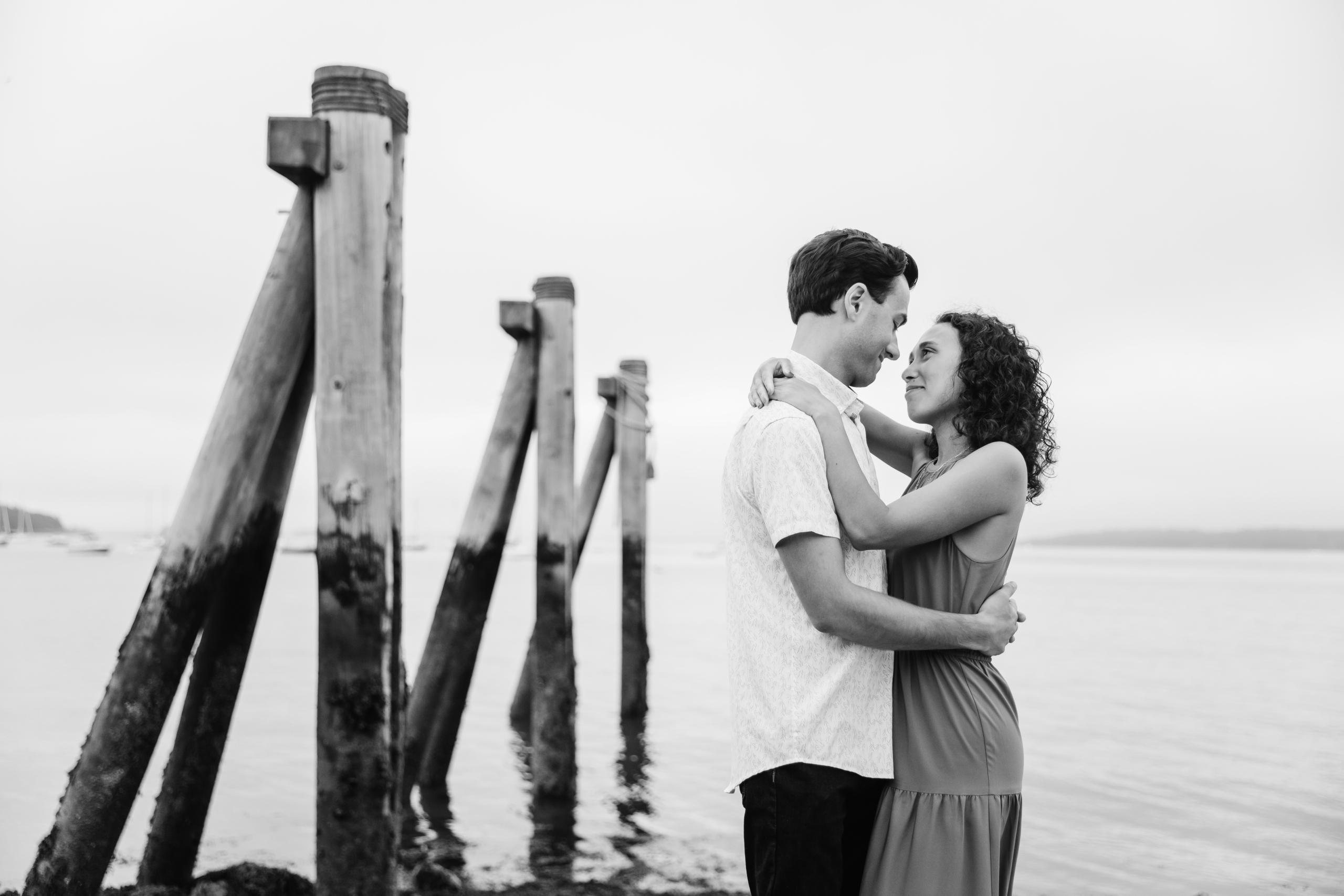 Logan and Cecilia embrace next to the dock posts at Eastern Promenade, in Portland, Maine